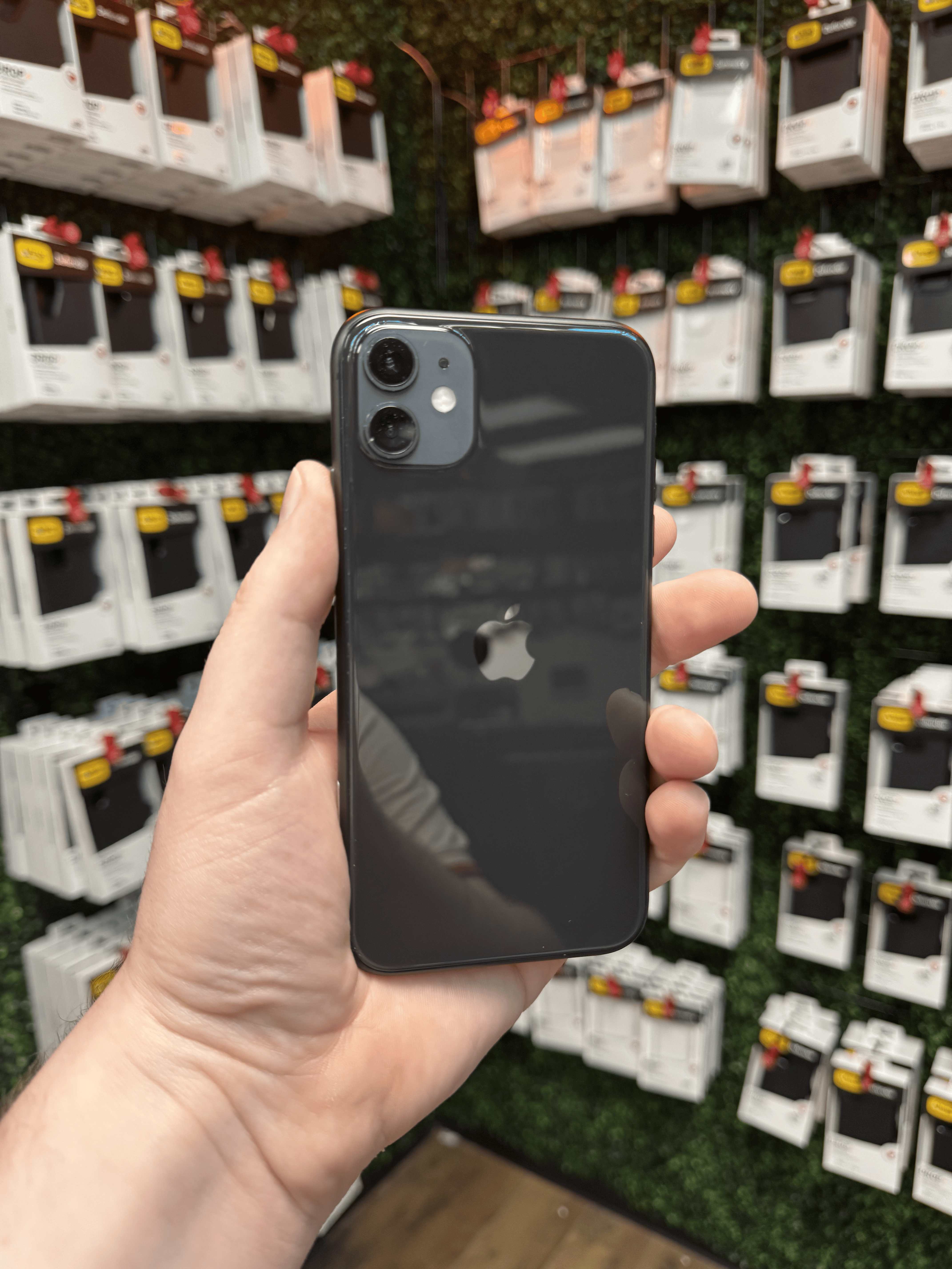 Fully restored iPhone 11 held in front of the Charlotte Tech Repair shop's accessory wall, ready to be returned to its owner