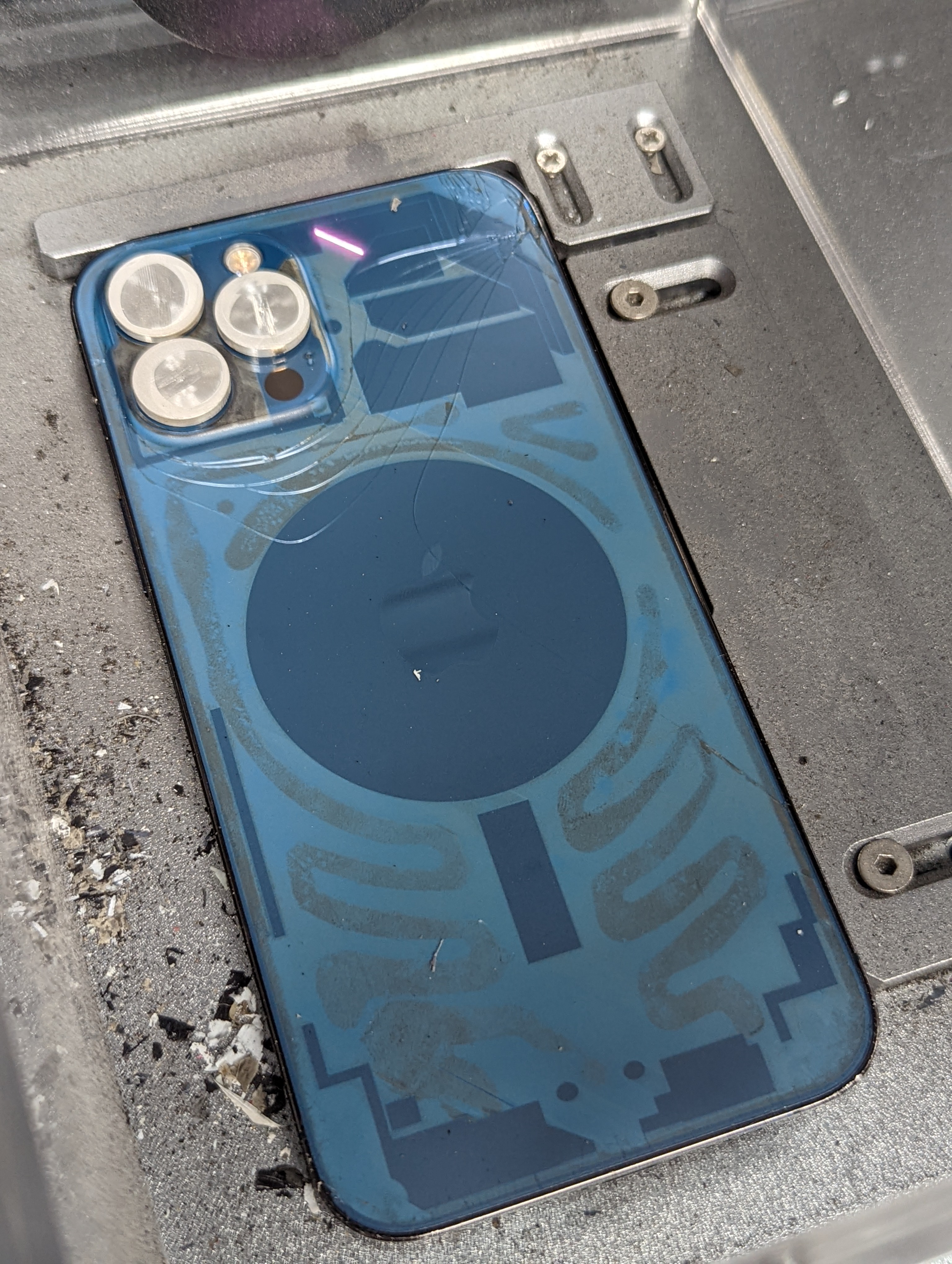 A Pacific Blue iPhone 12 Pro Max locked in the laser separator jig mid-treatment, with the laser line visible at the top and adhesive burn patterns across the lower glass