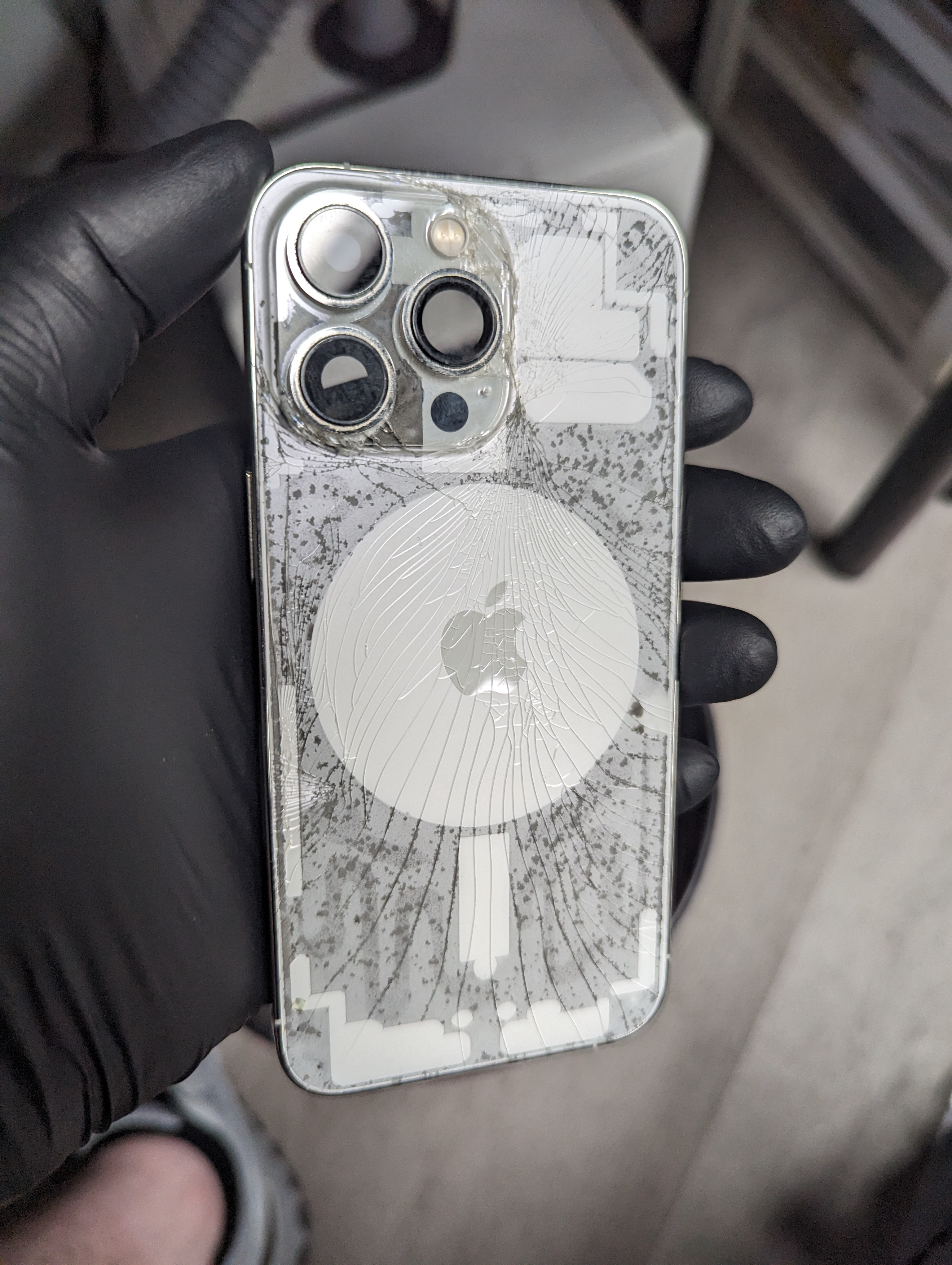 An iPhone back glass after a laser adhesive pass, showing the released adhesive pattern beneath the cracked glass