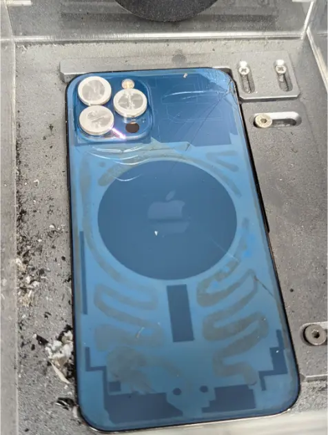 An iPhone back glass after a laser adhesive pass, showing the released adhesive pattern beneath the cracked glass