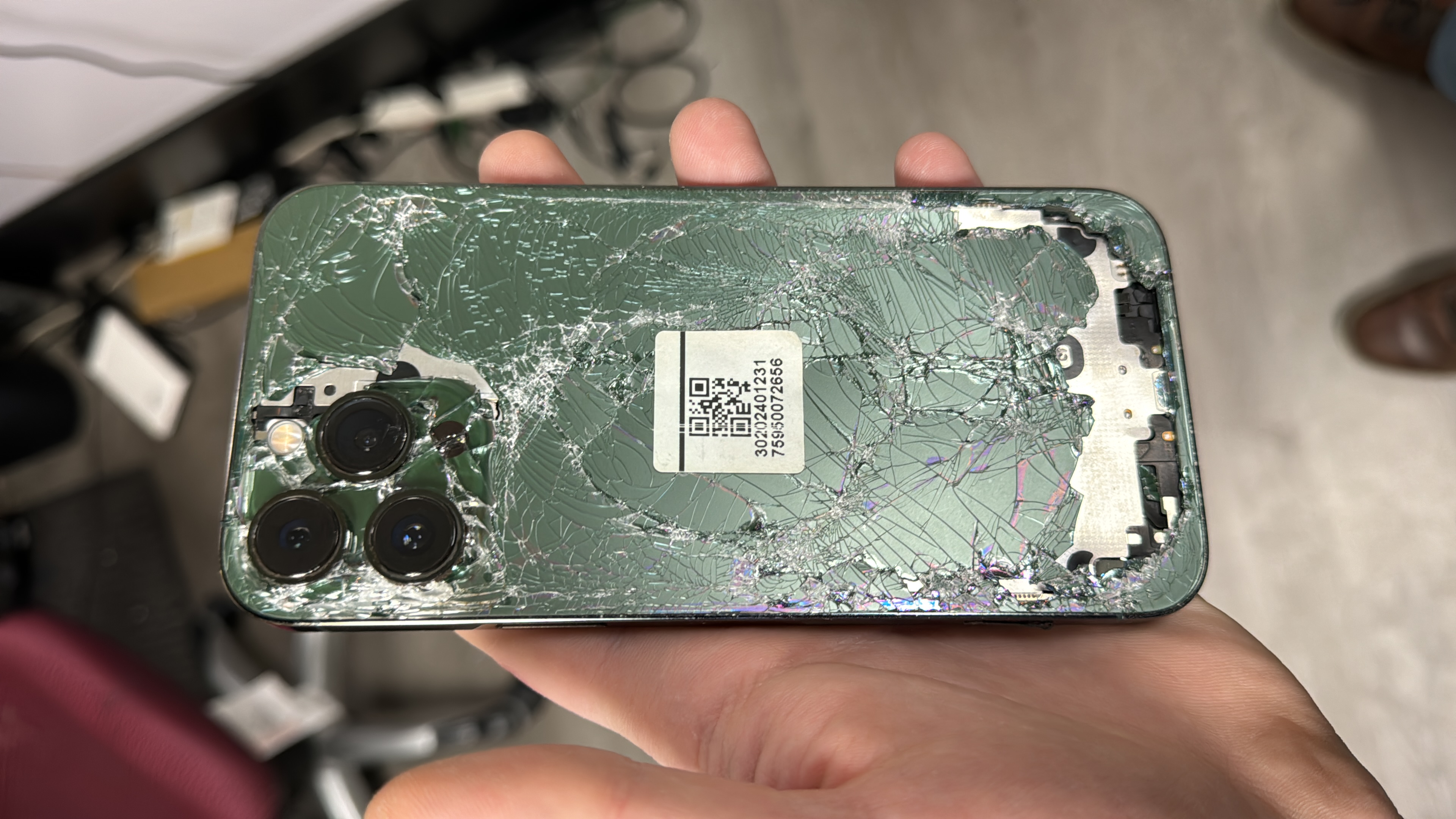 Severely shattered iPhone back glass with sections missing, exposing the internal components underneath