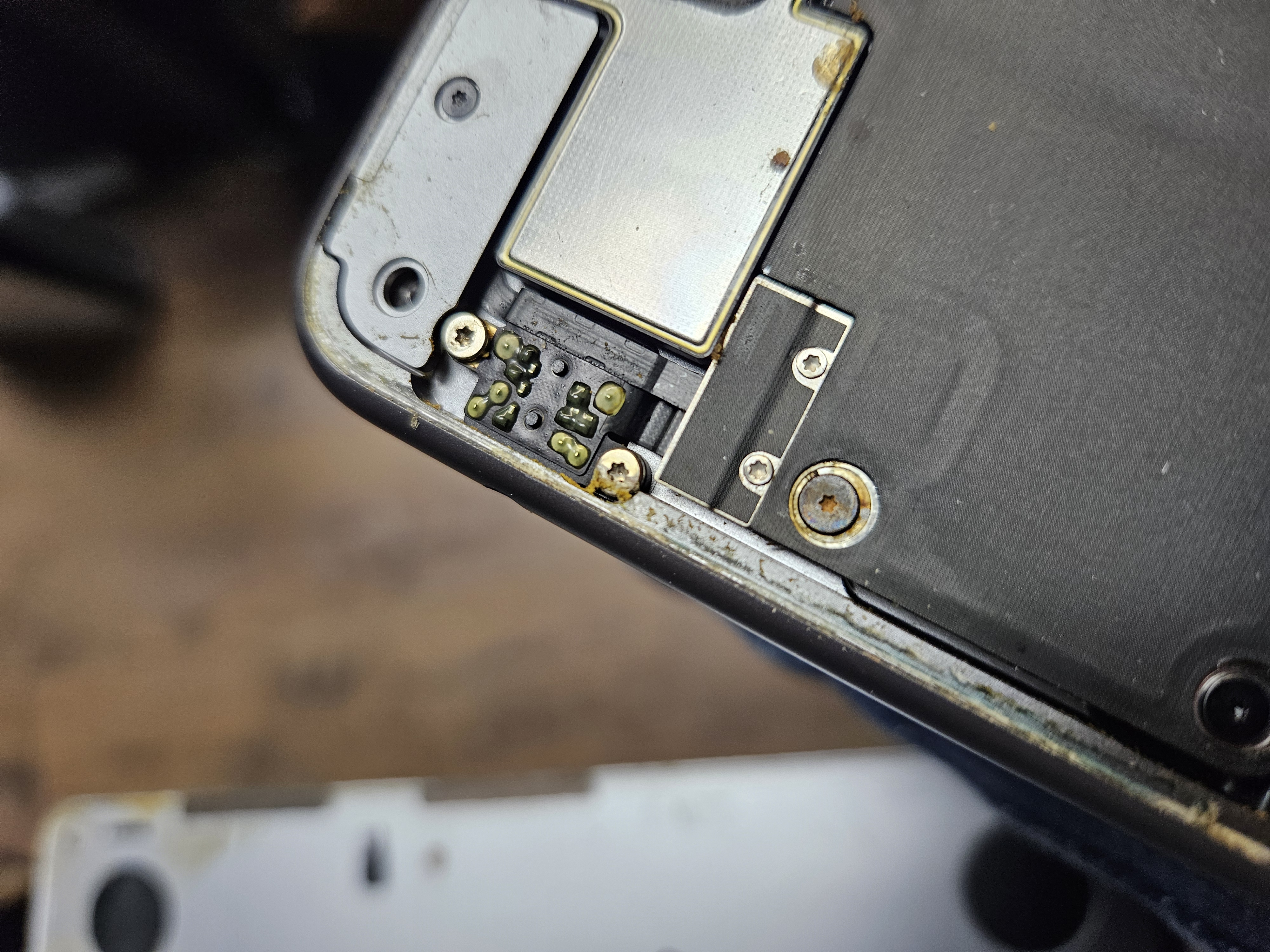 Close-up of corrosion on a MacBook logic board area and screw contacts caused by liquid damage