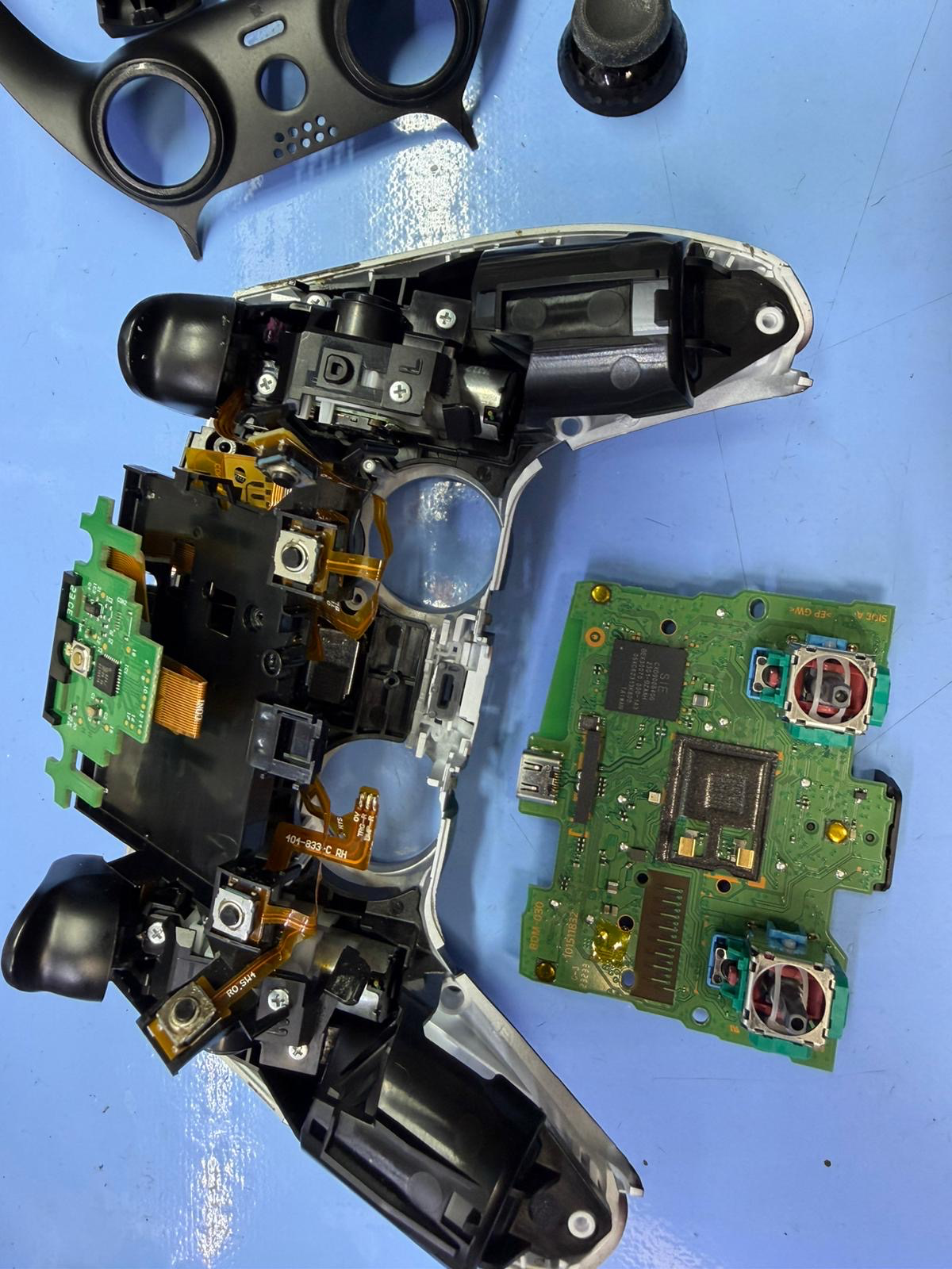 PS5 DualSense controller fully disassembled during stick drift repair at Charlotte Tech Repair — mainboard removed showing both analog stick modules and flex cables