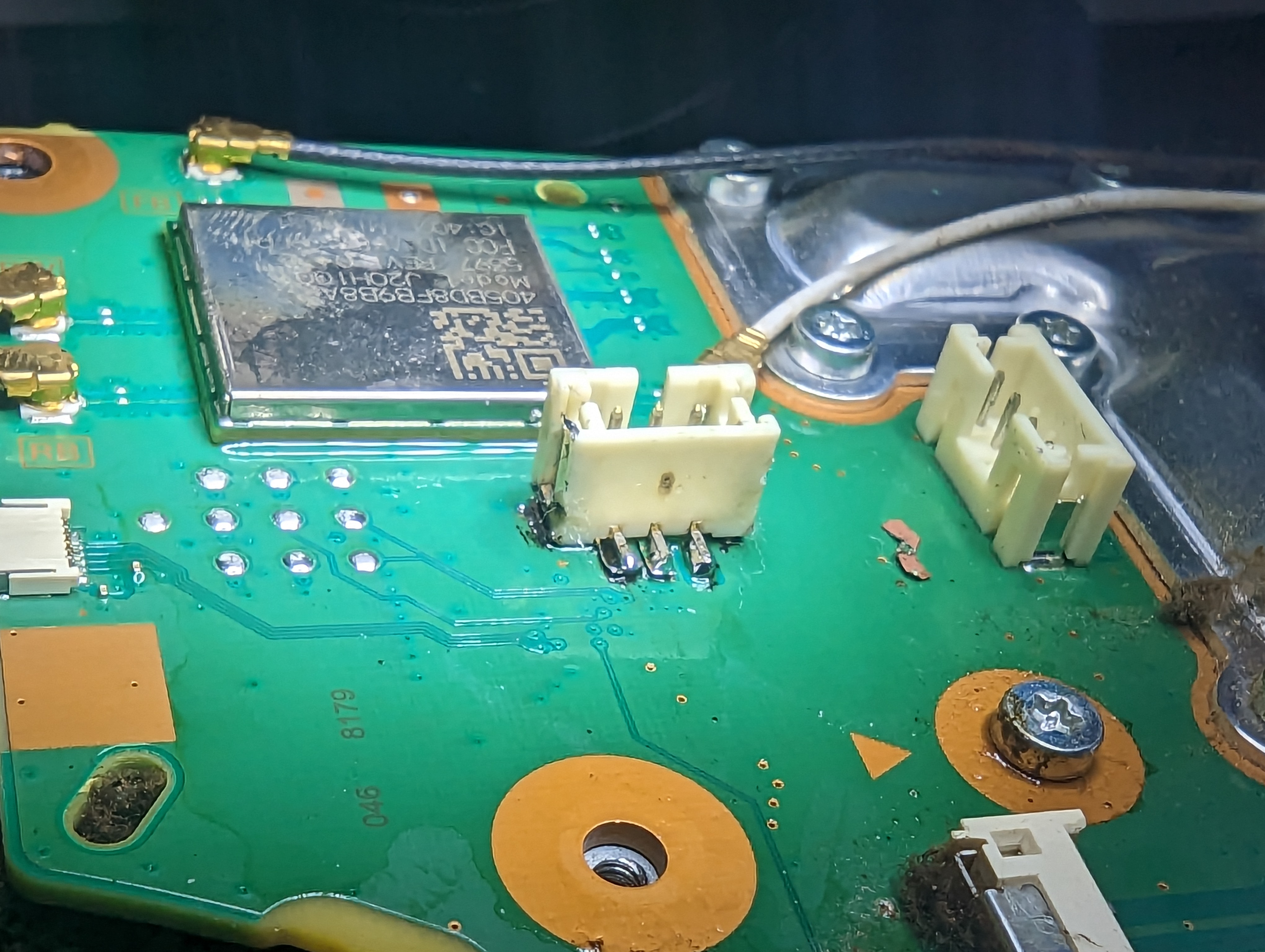 Close-up of a PS5 board connector with torn pads and a loose fragment of copper lying on the board