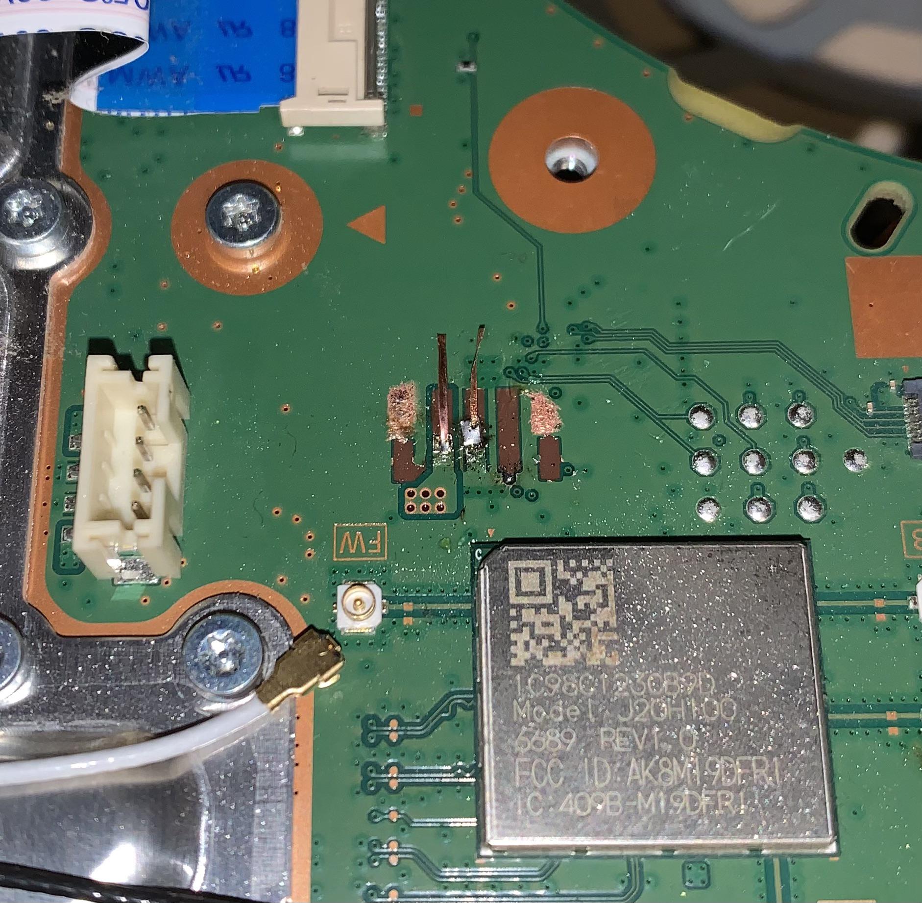 A PS5 motherboard where the fan connector has been torn off, leaving damaged pads and lifted traces