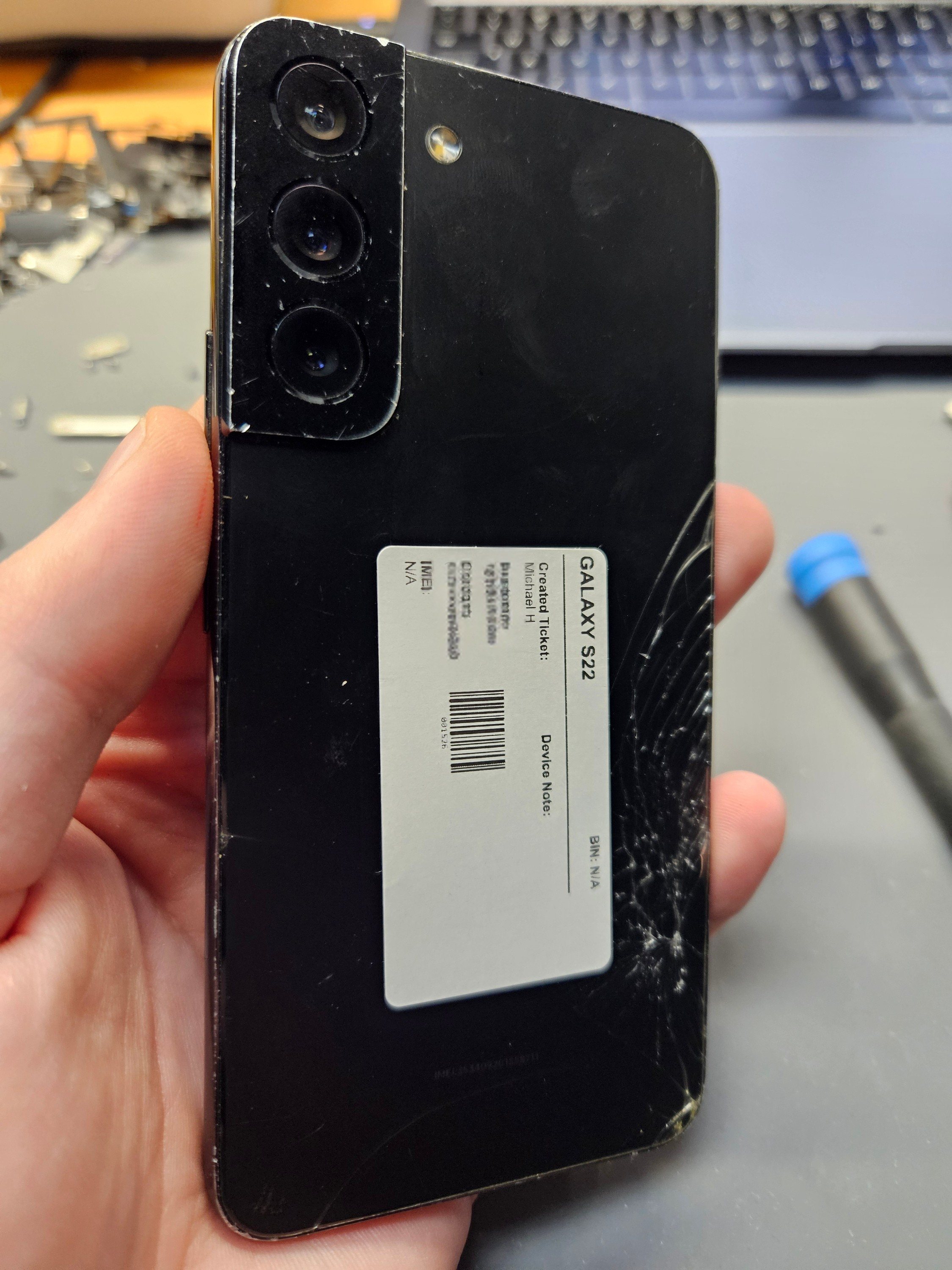 Cracked back glass on a Samsung Galaxy S22 held at the Charlotte Tech Repair bench, showing spider-web cracking across the lower corner